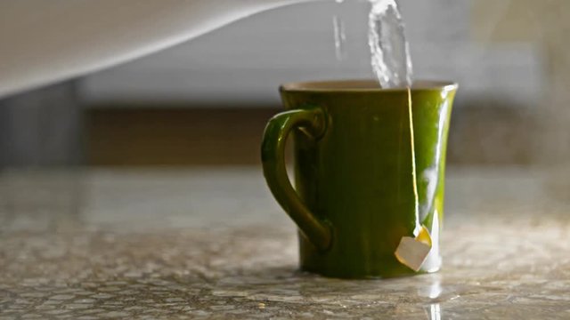 Add water in greem mug with tea bag and spill over some then dipping bag in mug