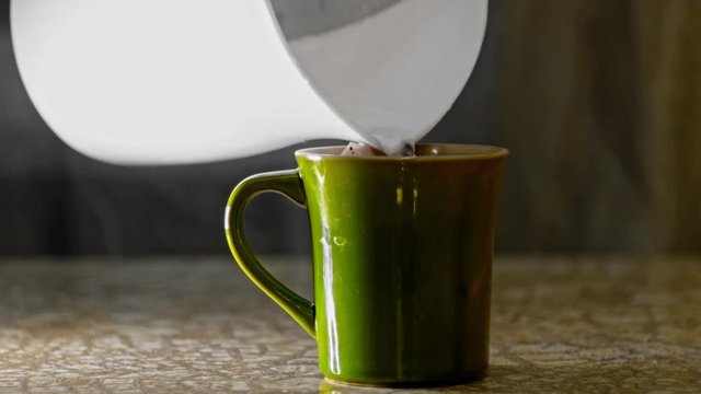 Adding some hot water from kettel into green mug then dipping tea bag