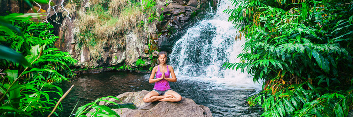Wellness yoga woman practicing meditation in nature by watefall and lush forest. Banner panorama of health and fitness, mindfulness concept.