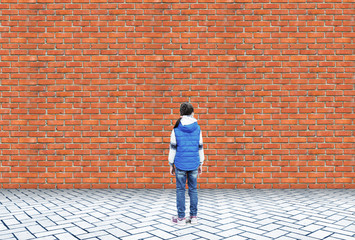Little girl stands in embarrassment in front of a high brick wall