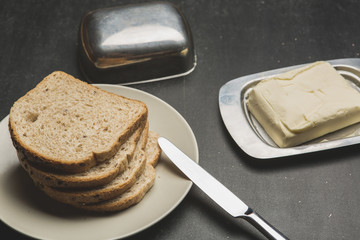 Plate with toasts and butter on dark table