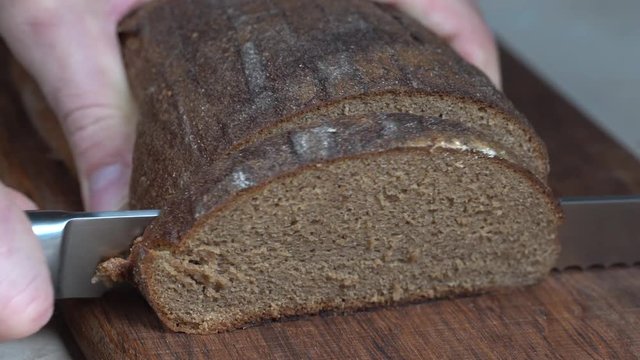Cutting slices of brown bread on wooden board. Cut the whole grain bread with a knife. Close up of dark bread, healthy lifestyle.