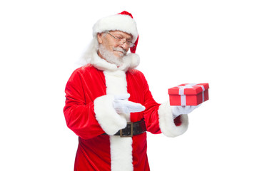 Christmas. Smiling Santa Claus in white gloves is holding a gift red box with a bow. Pointing at the gift. Isolated on white background.