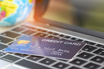 Mock up of credit card on laptop keyboard nearby globe. Consumers can buy products anywhere anytime from seller using web browser or application. Online shopping and e-commerce concept.