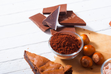 chocolate brownie cake and ingredients, baking papaer on white wood table background