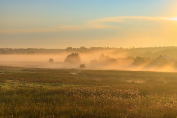 Fog over village houses in orange rays of rising sun in autumn morning. Nature landscape