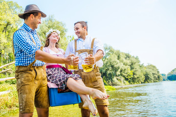 Oktoberfest Freunde in Lederhosen und Dirndl trinken Bier an der Isar