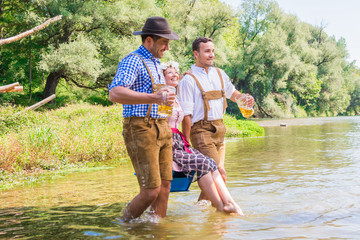 Oktoberfest Freunde in Lederhosen und Dirndl trinken Bier an der Isar