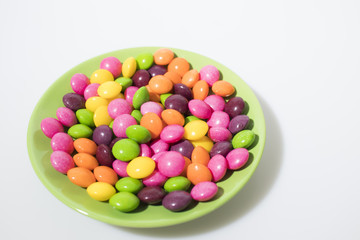 Many colored candies on a green plate isolated in a white background