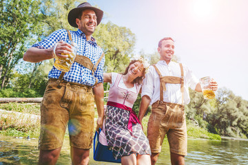 Oktoberfest Freunde in Lederhosen und Dirndl trinken Bier an der Isar