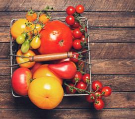 Colorful Organic Tomatoes in metal basket on wooden background with copy space. Fresh Red Yellow Orange and Green Tomatoes on wooden background. Retro styled. Top view.