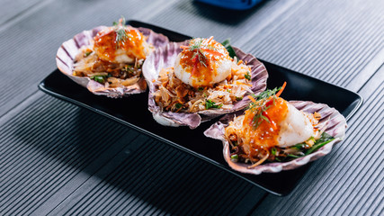 Grilled scallop in shell with spicy pomelo salad served in black plate.