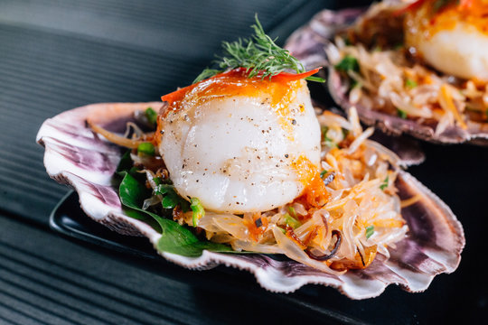 Close up Grilled scallop in shell with spicy pomelo salad served in black plate.