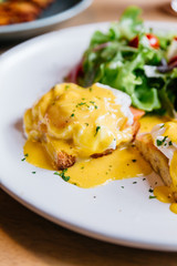 Close up Egg benedict served with salad in white plate on wooden table for delicious breakfast and brunch.