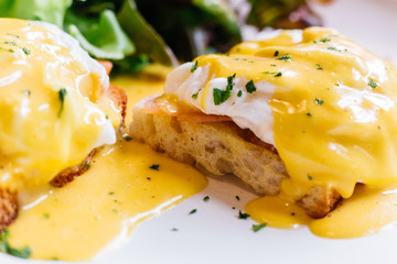Close up Egg benedict served with salad in white plate on wooden table for delicious breakfast and brunch.