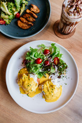 Top view of Egg benedict served with salad in white plate on wooden table for delicious breakfast and brunch.