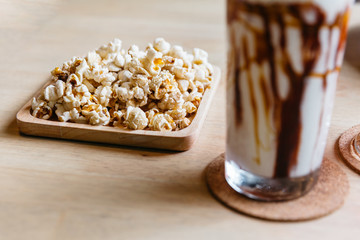 Salted popcorn served in wooden plate on square wooden table. 