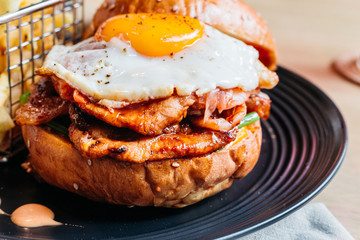 Tasty burger with fried egg served with fries in black plate on wooden table.