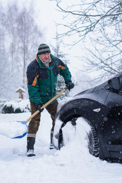 Winter, people and problem concept - closeup of man digging snow with shovel near car and yard. Man standing with blue shovel and he snow cleaning. Winter routine concept. 