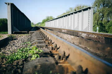 Rail tracks over the bridge in the green field. Railway transport industry. Empty road on summer day.