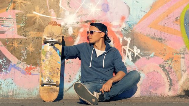 Person sits with a skateboard. A skater sits on a ground, holding a skateboard.