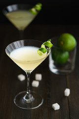 Two daiquiris served in cocktail glasses, garnished with lime zest. Dark wooden background, high resolution.