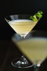 Two daiquiris served in cocktail glasses, garnished with lime zest. Dark wooden background, high resolution.