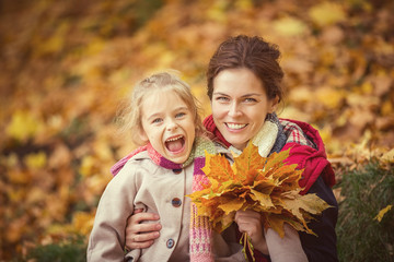 Happy little girl and her mother enjoy walk in autumn park and play with bright autumn leaves