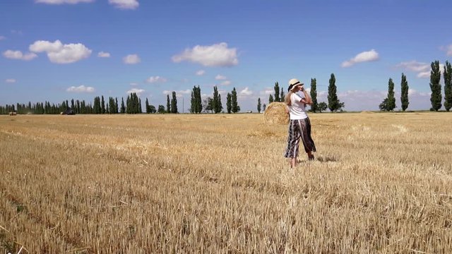 Young relaxed attractive female in casual clothes walking slowly on huge organic wheat field on hot summer day landscape