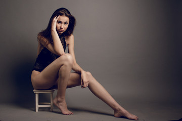 Fototapeta premium Young brunette female in black bra jeans and leather jacket over grey background