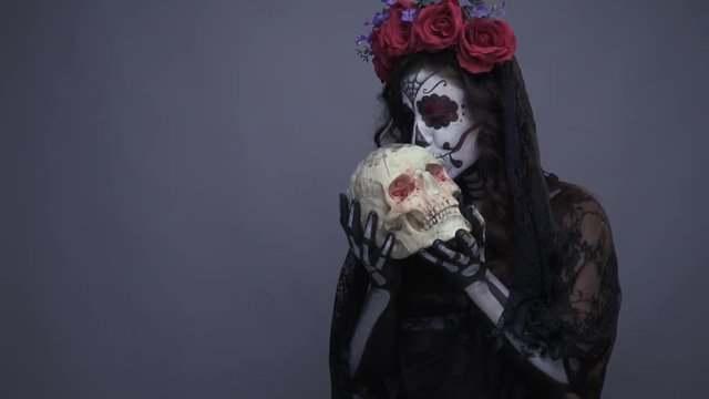 Girl on halloween in the image of the Mexican sugar skull kissing the skul