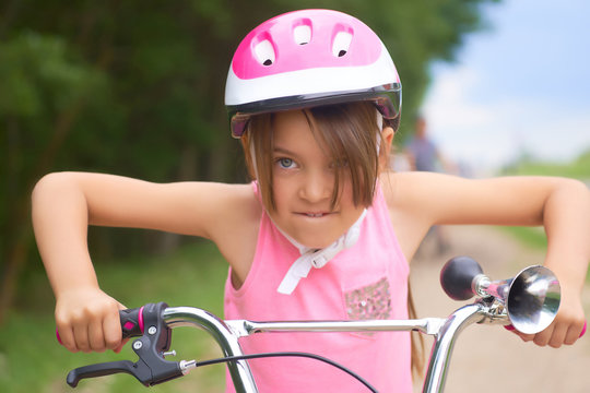Portrait of a litte girl in a pink safety helmet driving her bike.