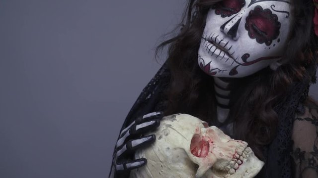 Dead girl holding a skull, make-up of a skeleton for halloween. Slow motion