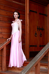 Fototapeta premium Fine emotional brunette on old style veranda, full length. Yonge girl in vintage pink pastel with live expressions on beautiful country and old background.