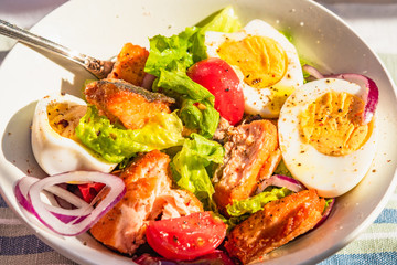 Paleo diet salad with salmon, tomatoes, eggs, onions and lettuce, close-up