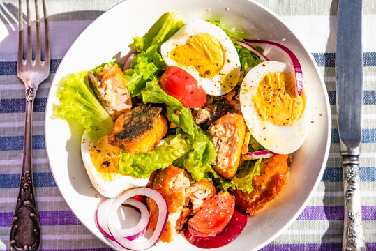 Paleo diet salad with salmon, tomatoes, eggs, onions and lettuce, top view