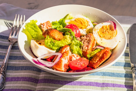 Paleo diet salad with salmon, tomatoes, eggs, onions and lettuce, top view