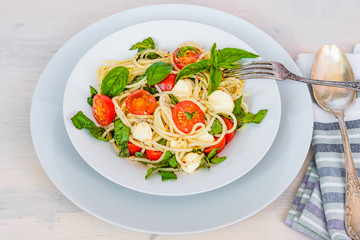 Italian food - Spaghetti caprese in a plate on a light rustic background, top view. Pasta with mozzarella, cherry tomatoes and basil