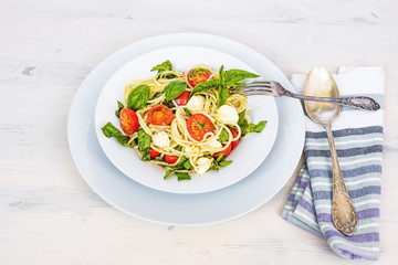 Italian food - Spaghetti caprese in a plate on a light rustic background, top view. Pasta with mozzarella, cherry tomatoes and basil