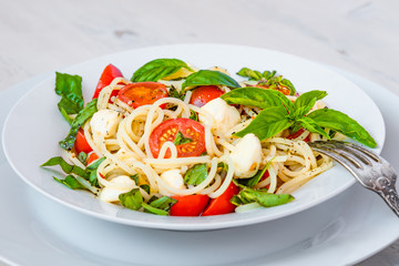 Spaghetti caprese - traditional Italian pasta with mozzarella cheese, cherry tomatoes and basil