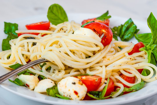 Spaghetti caprese - traditional Italian pasta with mozzarella cheese, cherry tomatoes and basil