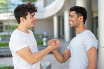 Cheerful young male friends meeting and greeting with handshake. Indian and Hispanic male student...