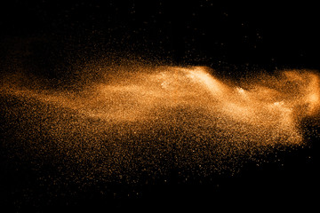 orange dust particles explosion on black background. Color powder dust splash.