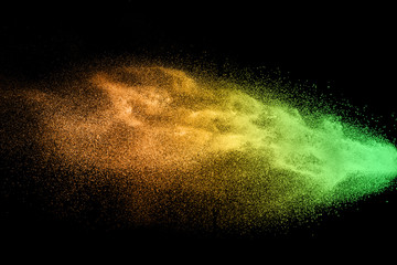 Green orange dust particles explosion on black background. Color powder dust splash.