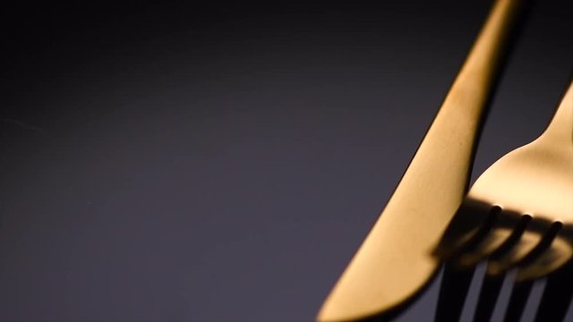 Luxury golden cutlery closeup. Knife and fork over black background. Rotation 360 degrees. 4K UHD video 3840x2160