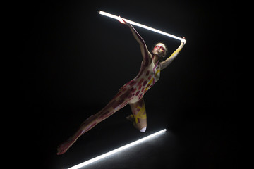 Mujer joven haciendo danza contemporánea con tubos de luces con el cuerpo pintado en un estudio de fotografía