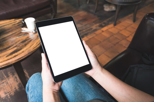 Mockup image of woman's hands holding black tablet pc with blank white desktop screen while sitting in cafe