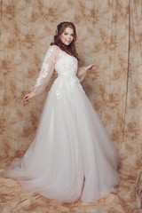 Fototapeta premium Beautiful and romantic bride in wedding dress with long sleeves. Young redheaded woman in wedding dress