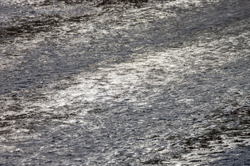 Background gray texture. The sun's rays are reflected from the asphalt covered with ice in winter.