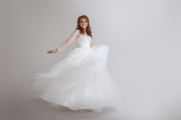 Fototapeta na wymiar Dancing young woman in wedding dress. Charming bride on Light background.